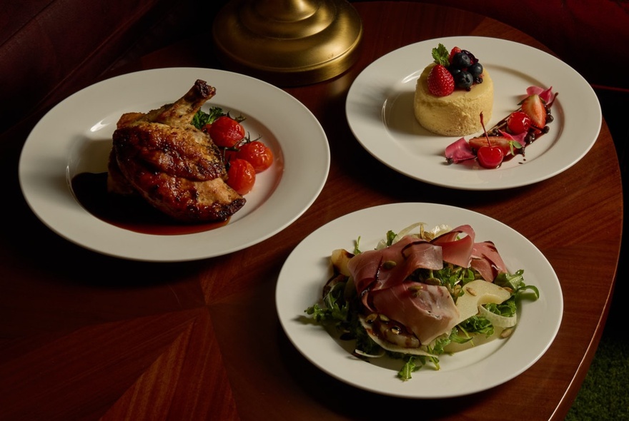 Three courses of a dinner service (entree, main and a dessert) on white plates on a wooden table.