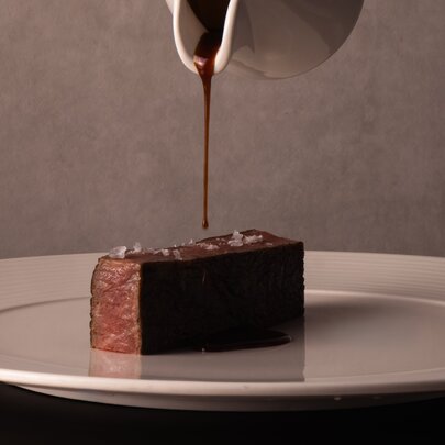 A perfectly rectangular piece of Wagyu steak in the centre of a white plate, gravy being poured onto it from a small, white gravy jug. 