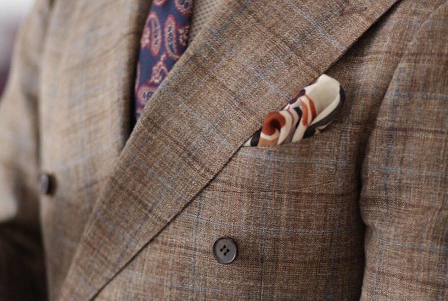 A close-up of a checked blazer with a patterned pocket handkerchief and a paisley tie. 