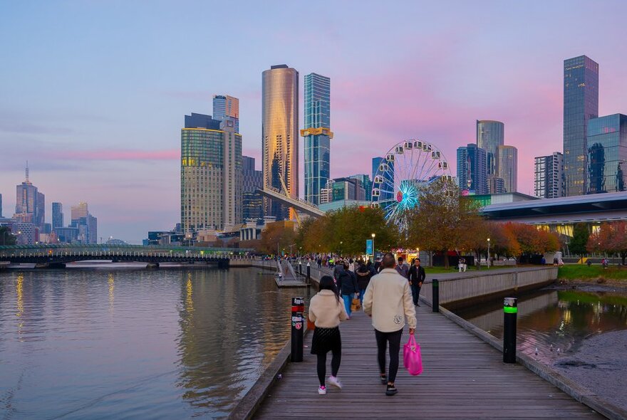 Two people are walking towards a Ferries wheel at sunset