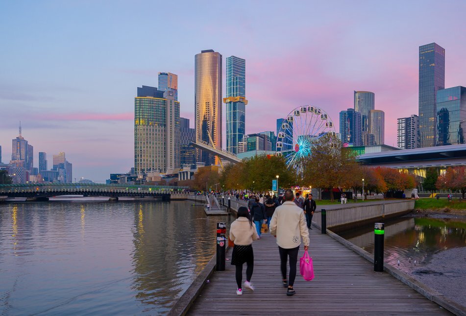 Two people are walking towards a Ferries wheel at sunset