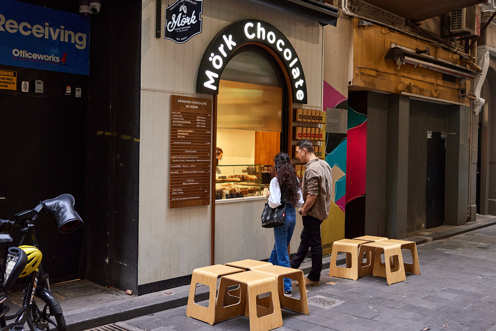 Two friends are ordering from a Mork Chocolate kiosk window