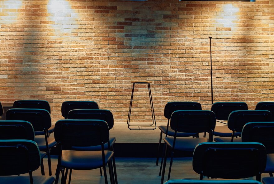 An intimate stage setting wth empty blue chairs and spotlights on the stage. 