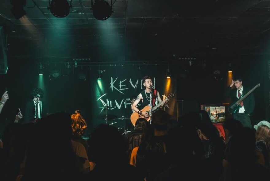 A band playing live on stage with an audience watching and listening.