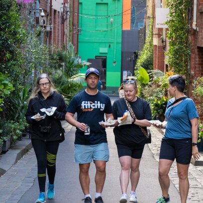 Three people walking with a Fit City tour guide through a leafy laneway in central Melbourne.