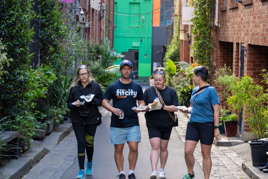 Three people walking with a Fit City tour guide through a leafy laneway in central Melbourne.