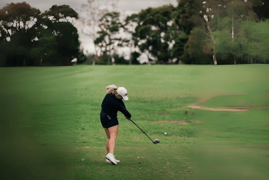 A person teeing off on a green with trees on the horizon.