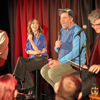 A group of improv comedians seated on a stage in front of an audience.
