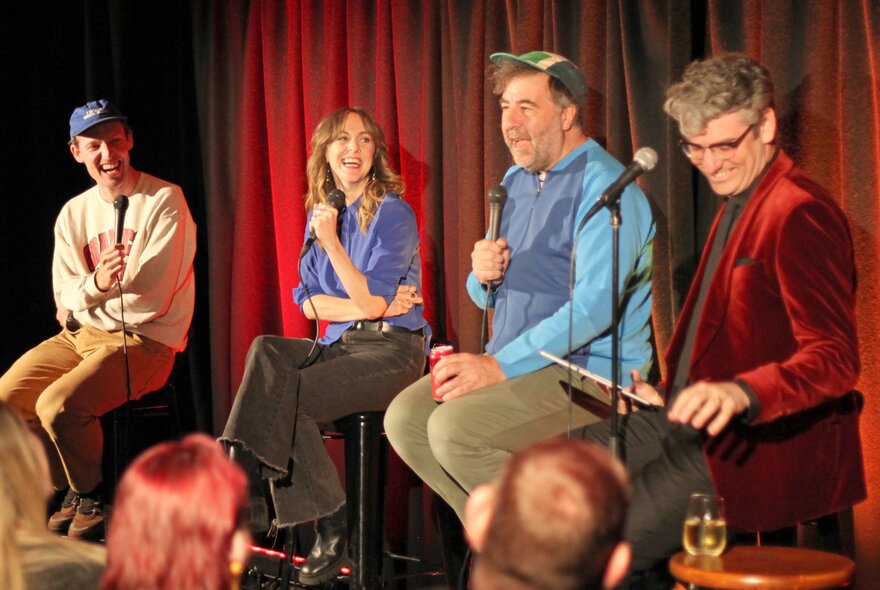 A group of improv comedians seated on a stage in front of an audience.