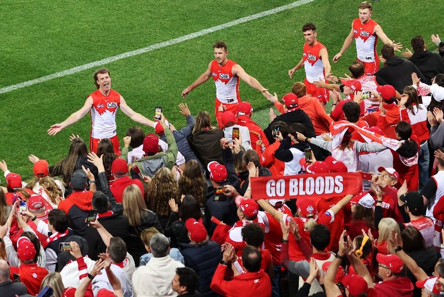 Sydney Swans players interacting with the crowd on the football field.