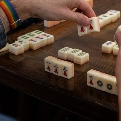 Hands arranging mahjong tiles on a table during a game.
