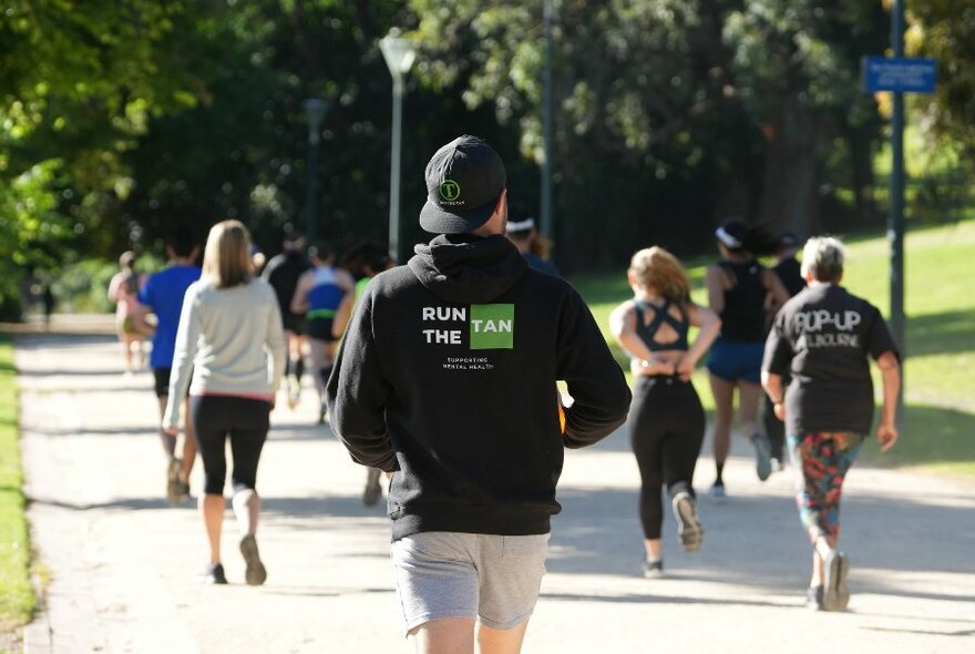 Looking at the backs of people on a running path in a park in the sun. 