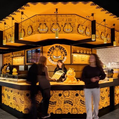 People milling around a yellow pop-up pizza bar with wraparound counter.
