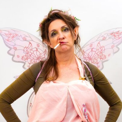 Woman dressed as a fairy smoking a cigarette and looking grumpy.