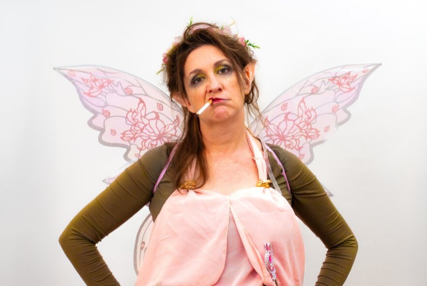 Woman dressed as a fairy smoking a cigarette and looking grumpy.