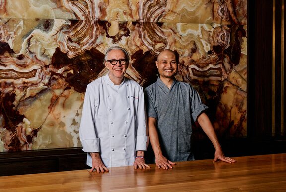 French Chef Philippe Mouchel and Warabi Chef Hajime Horiguchi standing next to each other, a marbled surface behind them.