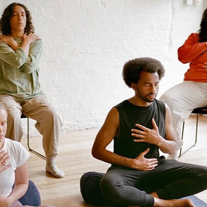 Four people in a wellbeing session, seated with hands on their chests and shoulders.