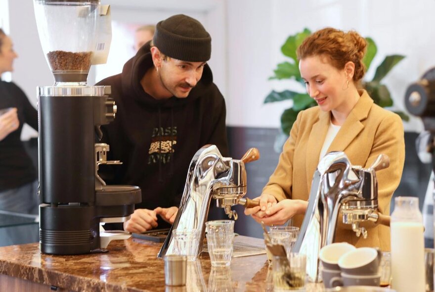 A customer learning how to make coffee with a barista and equipment.