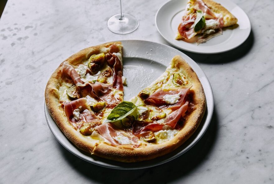 A pizza on a plate with a triangular slice on a smaller plate next to it.