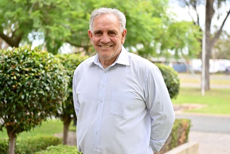 Smiling man standing in a driveway with clipped plants, lawn and trees.