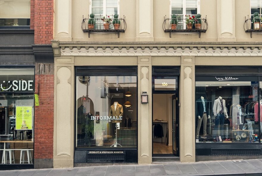 Building exterior of Informale men's clothing boutique, with large glass windows, and sandstone coloured bricks.
