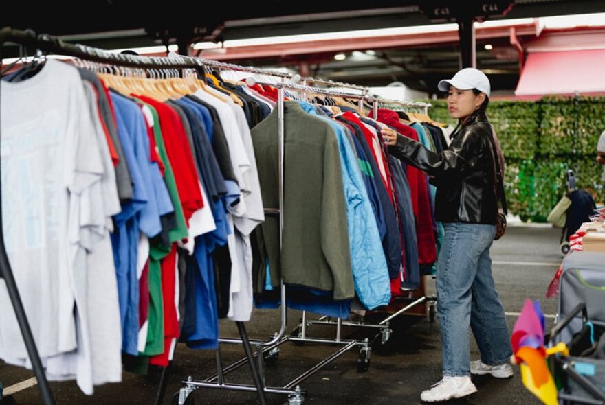 A woman looking through clothes hanging on a clothes rack at a stall in Queen Victoria Market.