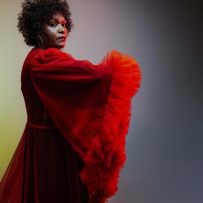 Singer Emma Donovan in a stunning red dress with fluffy trims looking serious over her right shoulder.