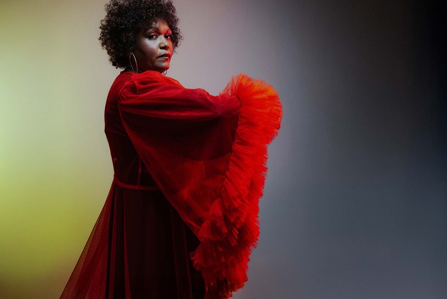 Singer Emma Donovan in a stunning red dress with fluffy trims looking serious over her right shoulder.