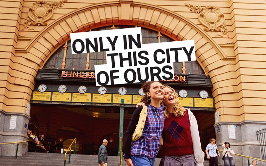 Two women smiling in front of Flinders Street Station clocks.