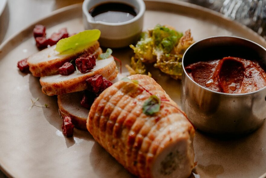 A dish of Christmas pork, with a sauce and side salad, on a large ceramic plate.