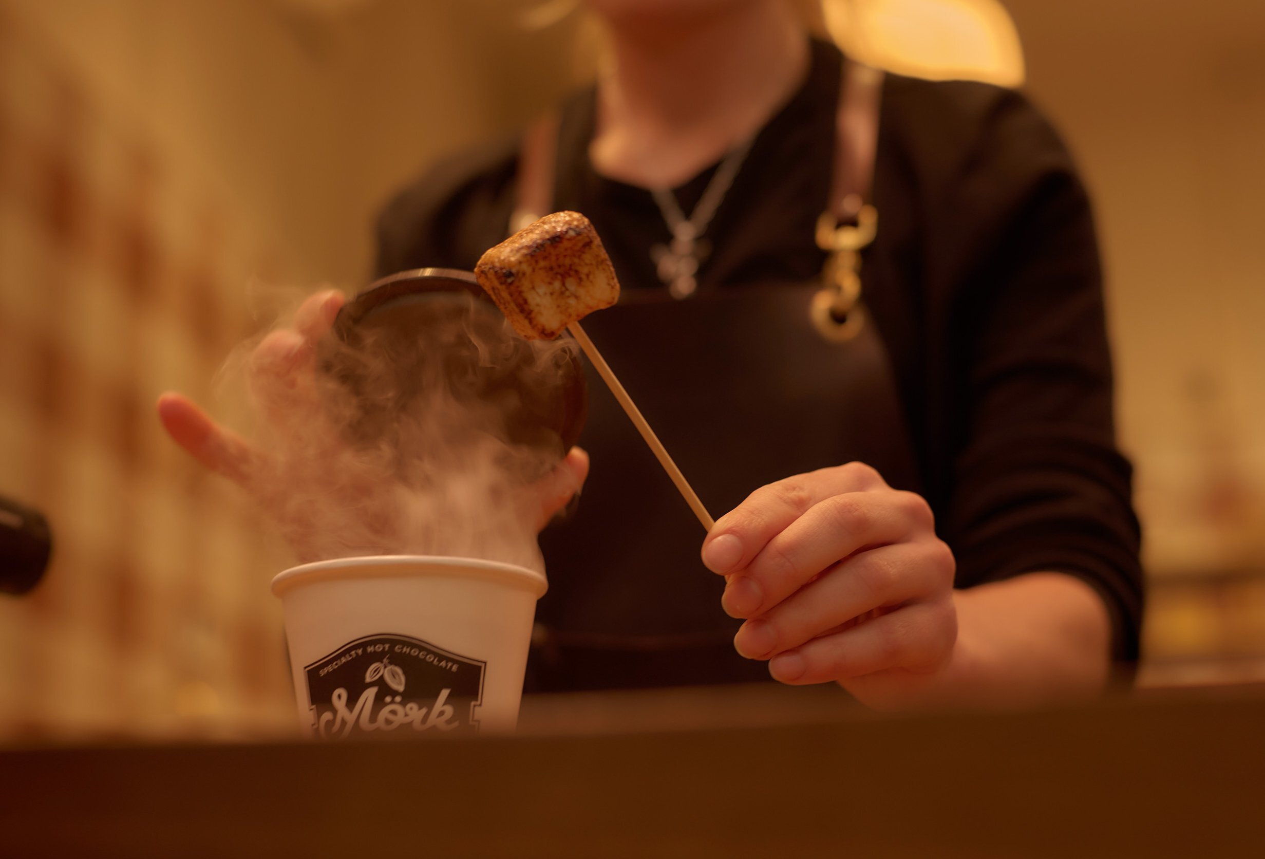 A cafe worker is making a hot chocolate with a marshmallow