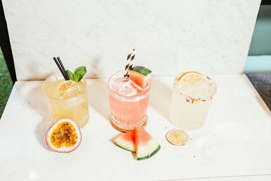 Three pastel-coloured cocktails in tumblers, with garnishes.