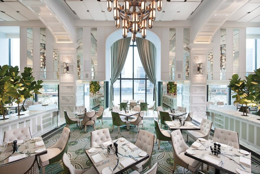 Luxury hotel buffet restaurant with high ceilings, art deco-style chandelier, marble and mirror walls, leafy plants, chic white and green furnishings and a large window with views of the Yarra River.