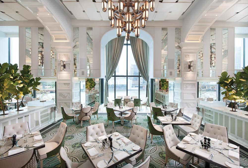 Luxury hotel buffet restaurant with high ceilings, art deco-style chandelier, marble and mirror walls, leafy plants, chic white and green furnishings and a large window with views of the Yarra River.