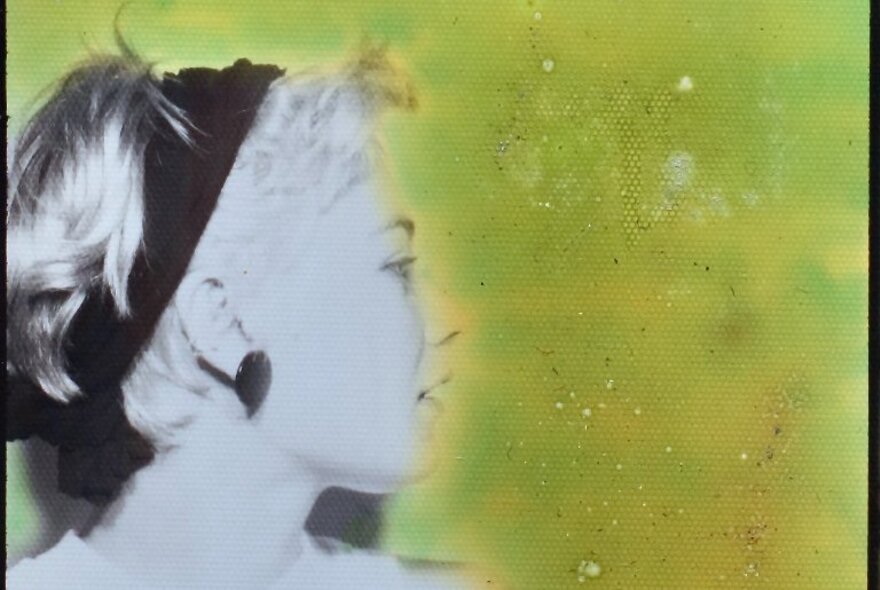A photobooth portrait of a woman facing the side, wearing a black headband from the 1980s; gelatin silver print with yellow ink.