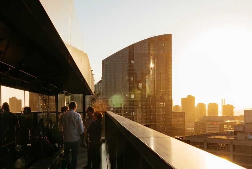 A rooftop bar with four people enjoying the sunset as it turns the city skyline gold.