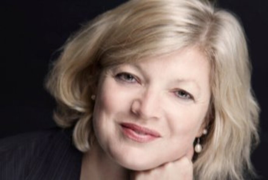 A headshot of Sian Prior, a woman with blonde hair, smiling slightly and wearing pearl earrings