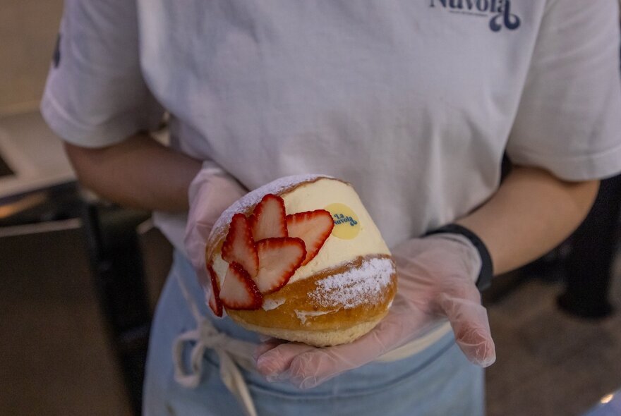 A person holding forth a maritozzi - cream filled brioche bun with strawberries. 