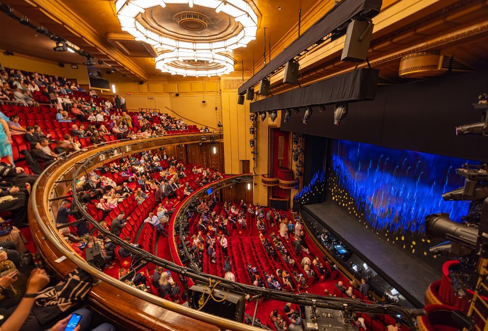 A grand theatre with red seats and large ring-shaped overhead lights.