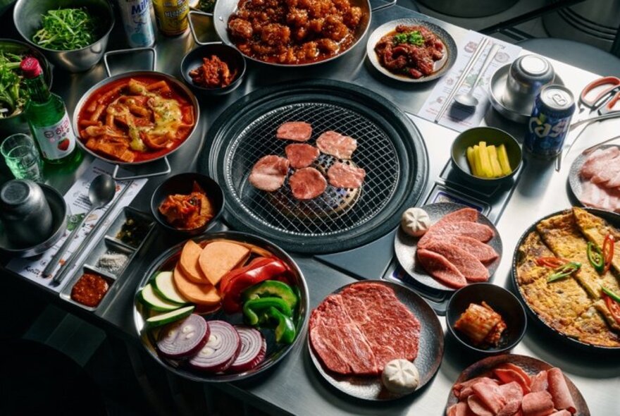 Table set with Korean grill, meat and accompanying dishes.