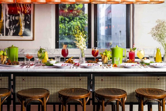A long bench table with stools, set for a girls-themed lunch event with pink cocktails and green water jugs.