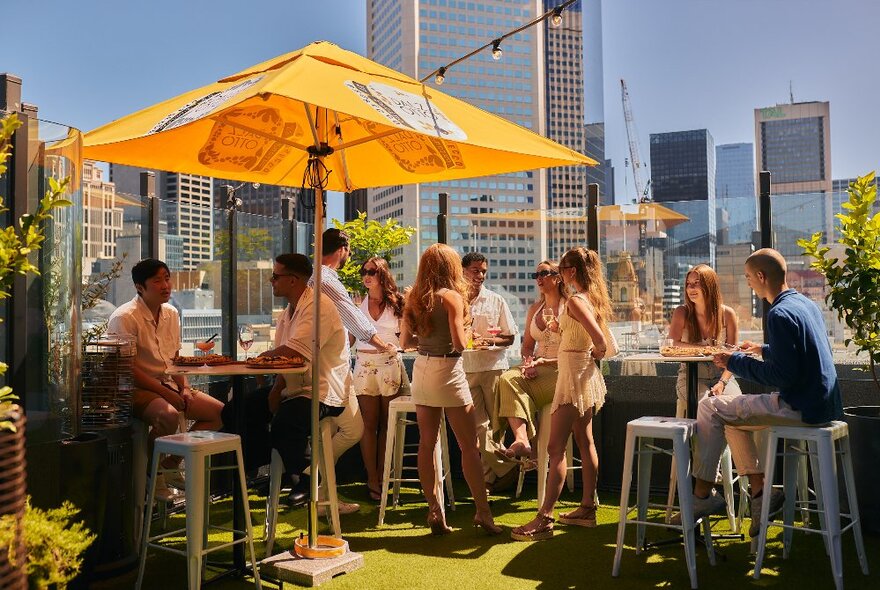 Young people enjoying the sunshine at a rooftop bar in Melbourne, the city skyline in the background.