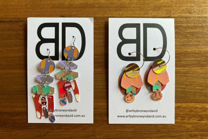 Two pairs of colourful earrings on display cards.