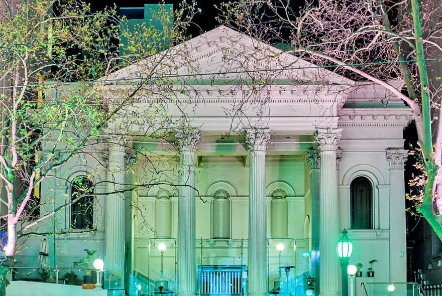 Collins St Baptist Church classical portico and pediment with trees at night.