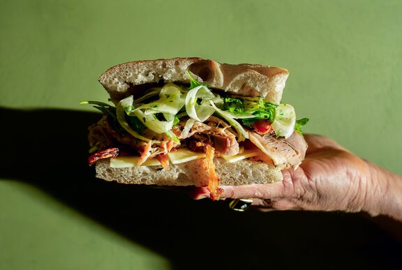 The porchetta panino with layers of roasted pork, cheese, fresh rocket in focaccia bread, held out on an open hand.