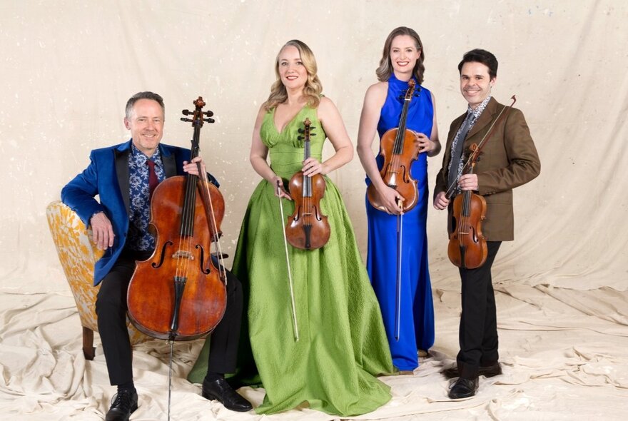 Musicians seated amd standing against a backdrop of flowing white material, holding stringed instruments.