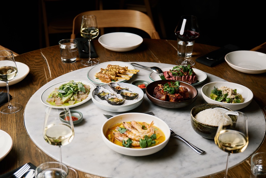 Restaurant setting with a vareity of dishes, cutlery and glasses of white wine.