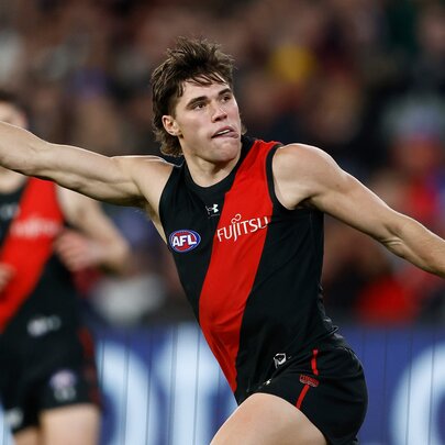 Essendon AFL football player stretching arms out to the side and pulling  aface.