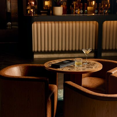 Interior of The Cliveden Bar & Dining at the Pullman East Melbourne, featuring elegant curved leather chairs and a textured bar front.