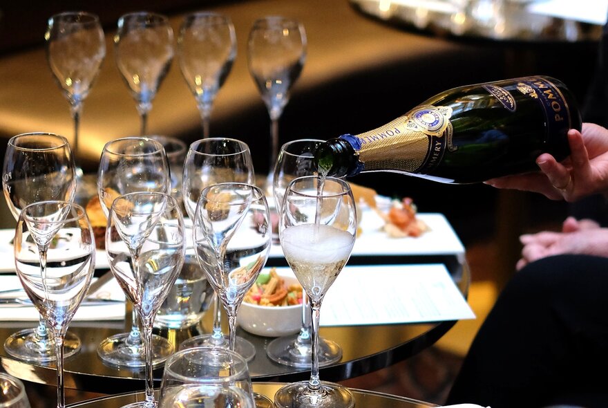 Twin rows of champagne glasses being expertly poured by a sommelier.
